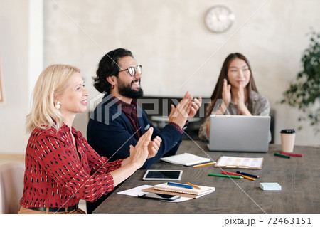 Happy intercultural professionals clapping their hands while sitting by table 72463151