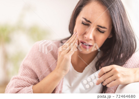 Pain in tooth while brunette holds her cheek with one hand, and painkilling pills in the other hand Pain in tooth while brunette holds her cheek with one hand, and painkilling pills in the other hand 72464680