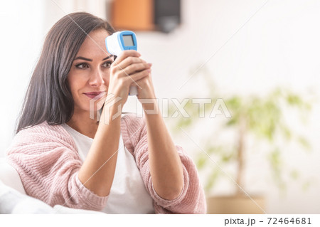 Woman self-measuring temperature with an infrared digital thermometer on her forehead Woman self-measuring temperature with an infrared digital thermometer on her forehead 72464681