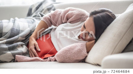 Woman falling asleep under the blanket on a couch after thermophore released the menstruation pain in her belly 72464684