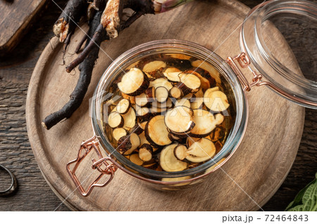 Sliced comfrey root in a glass jar - preparation of homemade tincture Sliced comfrey root in a glass jar - preparation of homemade tincture 72464843