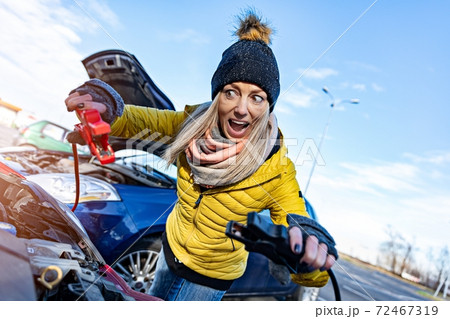 A terrified, furious blonde woman in a yellow jacket tries to recharge the discharged battery. 72467319