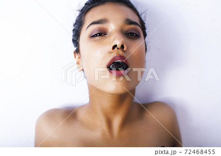 young pretty indian woman with dry fruit in mouth on white background young pretty indian woman with dry fruit in mouth on white background 72468455