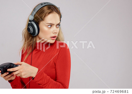 Woman with headphones Joystick in hands playing games fun leisure lifestyle entertainment red shirt gray background Woman with headphones Joystick in hands playing games fun leisure lifestyle entertainment red shirt gray background 72469681