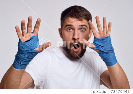 A sportive man in a white T-shirt boxing bandages on his hands practicing blow exercises improving skills A sportive man in a white T-shirt boxing bandages on his hands practicing blow exercises improving skills 72470445