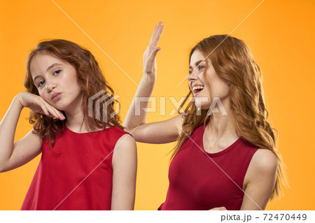 Happy sisters in red dresses on a yellow background are having fun and gesticulating Copy Space 72470449