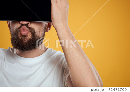 Portrait of a man with a tablet in front of his face on a yellow background cropped view of a white T-shirt Copy Space Portrait of a man with a tablet in front of his face on a yellow background cropped view of a white T-shirt Copy Space 72471709