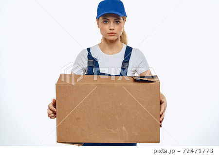A woman in a working uniform with a box in the hands of a delivery service delivery service light background A woman in a working uniform with a box in the hands of a delivery service delivery service light background 72471773