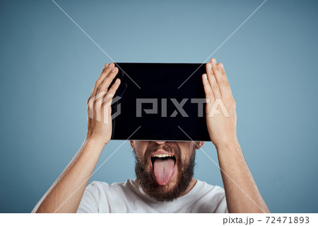 man with touch tablet in front of face on blue background cropped view copy space emotions model 72471893