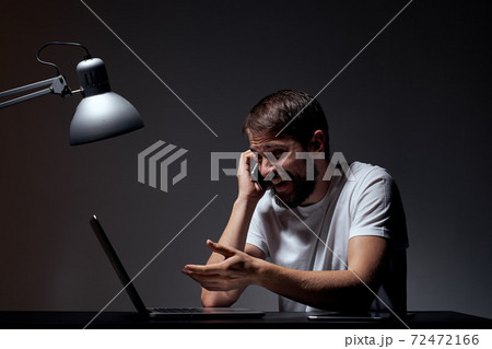 man with laptop sitting at table dark background workplace office emotions lamp gesturing with hands model cropped view 72472166