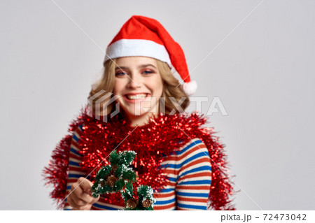 emotional woman with branches of a festive tree and red tinsel cap on her head striped sweate emotional woman with branches of a festive tree and red tinsel cap on her head striped sweate 72473042