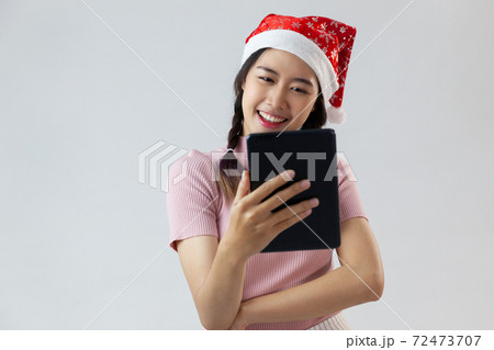 Attractive young businesswoman with pretty smile wearing santa hat looking at camera a digital tablet computer with a surprise and chatting posed 72473707