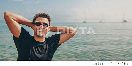 a contented man in sunglasses with his hands behind his head by the water. vacation by the sea. Refreshing treatments 72475167