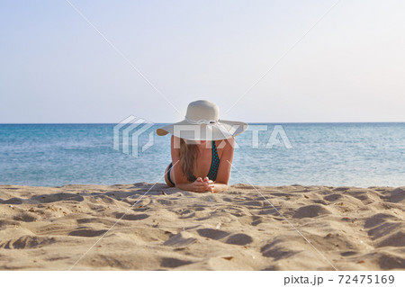 journey to the sea. girl in a bathing suit and hat sunbathing on the beach. tourist sitting on the sand. leisure wear. copy space journey to the sea. girl in a bathing suit and hat sunbathing on the beach. tourist sitting on the sand. leisure wear. copy space 72475169