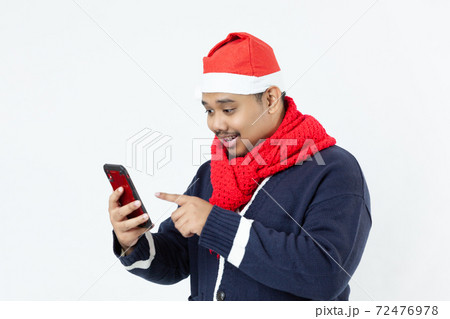 Portrait young asian man in blue sweater, red santa hat and red scarf using smartphone to shopping online and chatting on the white background 72476978