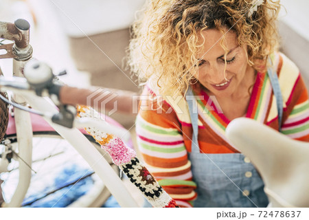 Close up portrait of cheerful beautiful caucasian middle age blonde woman at home working on a coloured bike - home activity work for happy and alternative people 72478637