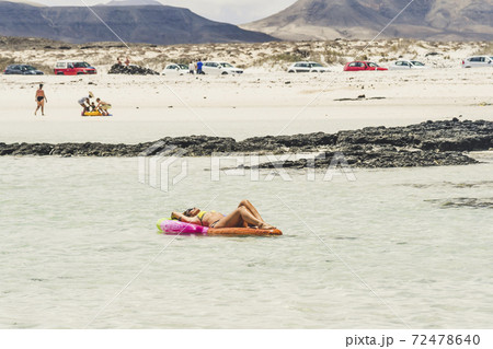 Tourism and tourists concept in summer holiday vacation - nice woman enjoying sunbath on a coloured lilo in the sea water at the beach with people in background 72478640