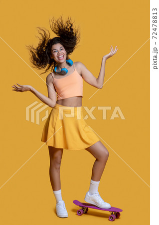 Pretty dark-haired young girl with a skateboard looking joyful 72478813