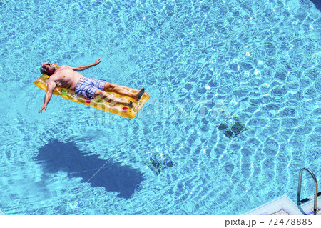 Retired lifestyle beautiful man senior age relaxing and enjoying the blue water pool sleeping on a orange coloured trendy lilo in summer holiday vacation - concept of relax in retired life 72478885