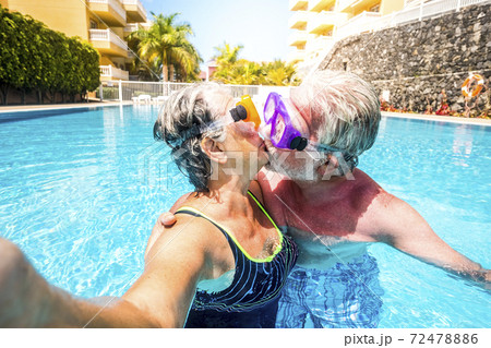 Concept of no limit age and relationship with couple of caucasian happy senior old people kissing together in the pool having fun during summer holiday vacation 72478886