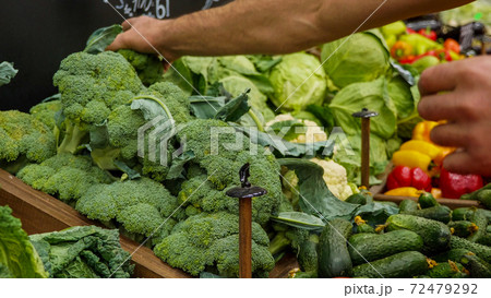 Close-up hands of grocery worker is arranging vegetables on store shelves. Close-up hands of grocery worker is arranging vegetables on store shelves. 72479292
