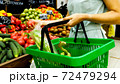 Woman with shopping basket is choosing vegetables in grocery store. 72479294