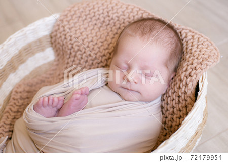 Cute little baby in a knitted hat with a toy bunny lies in a wicker basket decorated with greens and lemons in a beige knitted blanket. Summer mood. Happy healthy childhood 72479954