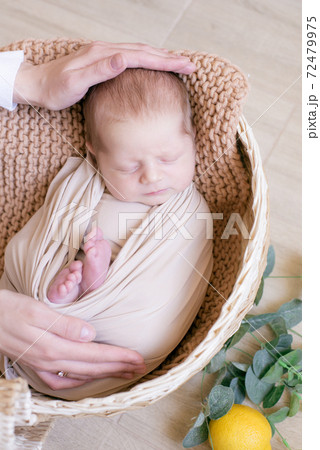 Cute little baby in a knitted hat with a toy bunny lies in a wicker basket decorated with greens and lemons in a beige knitted blanket. Summer mood. Happy healthy childhood Cute little baby in a knitted hat with a toy bunny lies in a wicker basket decorated with greens and lemons in a beige knitted blanket. Summer mood. Happy healthy childhood 72479975