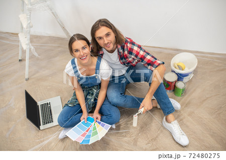 Young couple sitting on the floor and choosing a color for paint 72480275