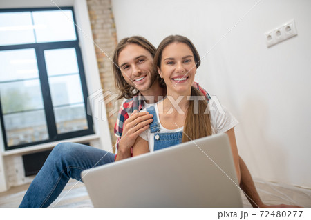 Young couple sitting on the floor and searching for something online 72480277