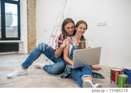 Young couple sitting on the floor and searching for something online 72480279