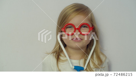 Funny little child girl wear red glasses holding stethoscope playing game as doctor, happy cute adorable small preschool kid pretending medic nurse looking at camera, close up portrait. Funny little child girl wear red glasses holding stethoscope playing game as doctor, happy cute adorable small preschool kid pretending medic nurse looking at camera, close up portrait. 72486215