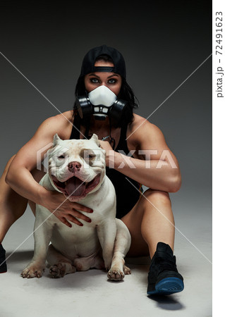 Young sporty woman in medical mask hugs her dog american bully. Pandemic. Coronavirus concept. Health protection during covid-19 outbreak Young sporty woman in medical mask hugs her dog american bully. Pandemic. Coronavirus concept. Health protection during covid-19 outbreak 72491623