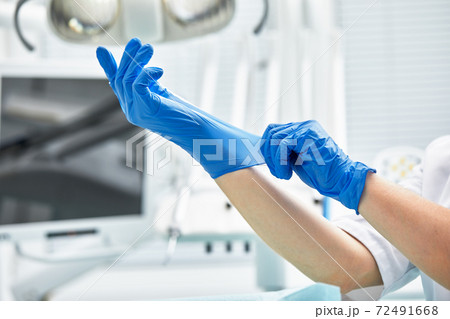 A female dentist puts on gloves against a background of dental equipment in a dental office. Happy patient and dentist concept. 72491668