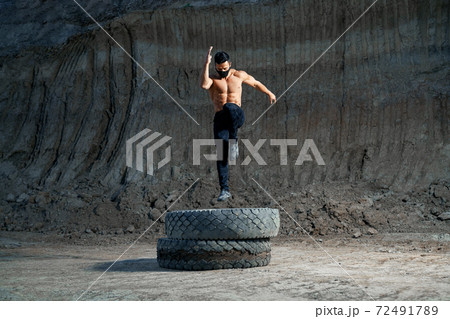 Handsome strong man jumping on wheel during evening workout Handsome strong man jumping on wheel during evening workout 72491789