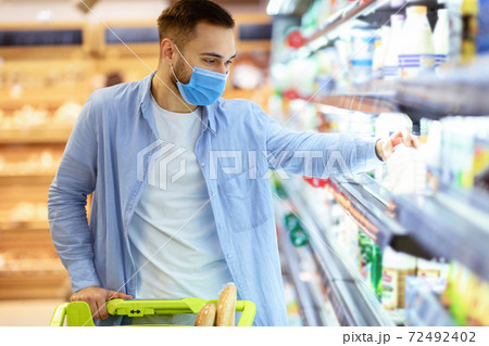 Man in medical mask shopping in supermarket taking milk 72492402