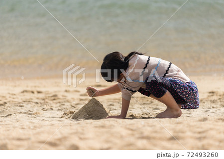 初夏の海の砂浜で砂遊びをしている可愛い子供の姿の写真素材