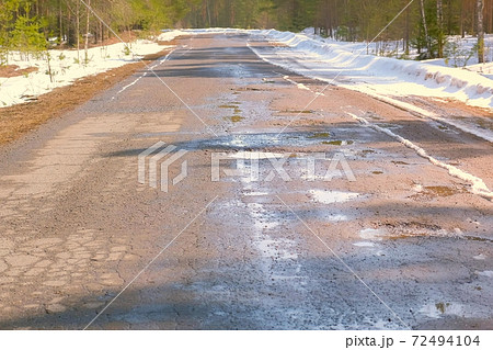 Destroyed broken asphalt road with holes, melting snow and puddles early spring. 72494104