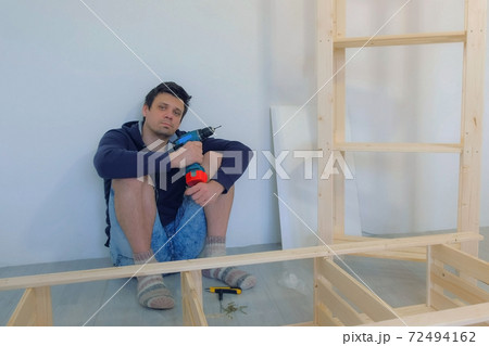 Man sitting on floor resting with electric screwdriver in hands collecting rack. Man sitting on floor resting with electric screwdriver in hands collecting rack. 72494162