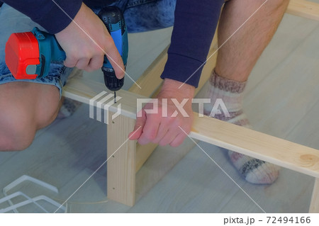 Man screws boards using electric screwdriver collecting rack furniture bookcase. Man screws boards using electric screwdriver collecting rack furniture bookcase. 72494166