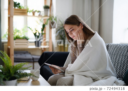 Worried young woman with blanket using tablet at home, coronavirus concept. Worried young woman with blanket using tablet at home, coronavirus concept. 72494318
