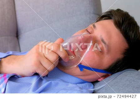 Sick man in oxygen mask due to difficulty in breathing in coronavirus pandemic. 72494427
