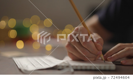 closeup man writes Shopping list in notepad with a pencil under warm light in the evening with medicine mask near hand closeup man writes Shopping list in notepad with a pencil under warm light in the evening with medicine mask near hand 72494604