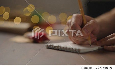 man writes christmas gifts in notepad with a pencil under warm light in the evening man writes christmas gifts in notepad with a pencil under warm light in the evening 72494619