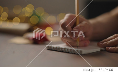 man writes christmas gifts in notepad with a pencil under warm light in the evening man writes christmas gifts in notepad with a pencil under warm light in the evening 72494661