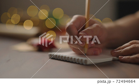 man writes christmas gifts in notepad with a pencil under warm light in the evening man writes christmas gifts in notepad with a pencil under warm light in the evening 72494664
