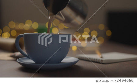 man pour hot chocolate in blue cup in the evening with shopping list for holidays in notepad 72494666