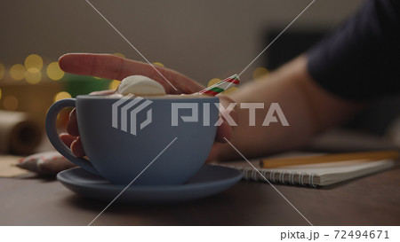man drinking hot chocolate from blue cup in the evening making shopping list for holidays 72494671