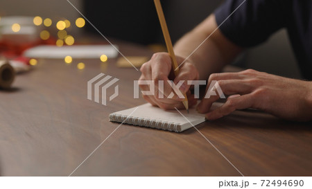 man writes christmas gift list for holidays in notepad with a pencil under warm light in the evening 72494690