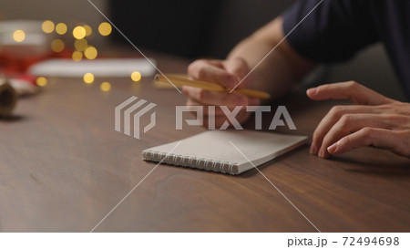 man writes christmas gift list for holidays in notepad with a pencil under warm light in the evening man writes christmas gift list for holidays in notepad with a pencil under warm light in the evening 72494698